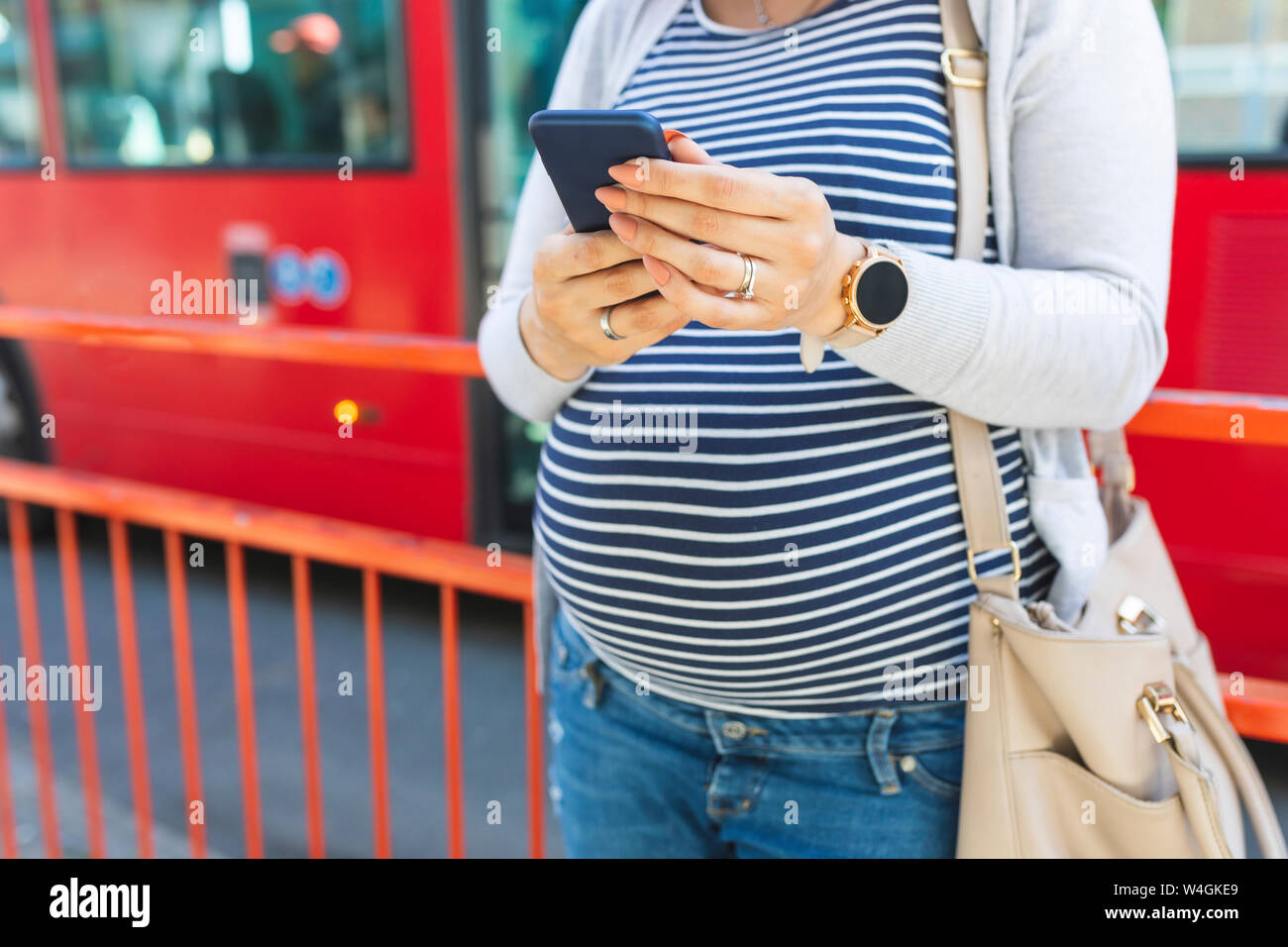 Donna incinta utilizzando il suo telefono esterno Foto Stock