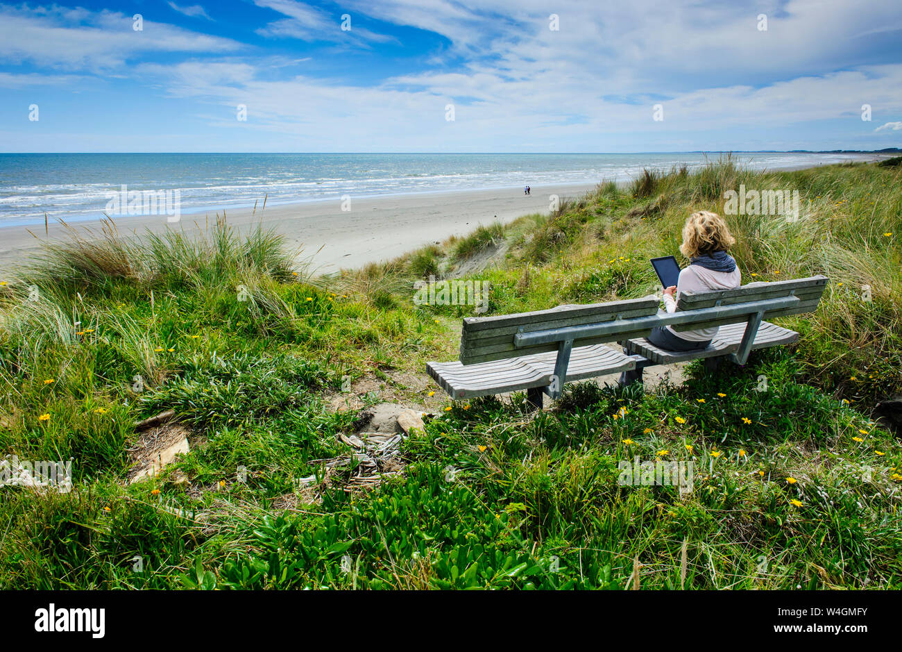 Donna seduta su una panchina con tablet a Foxton beach, la Costa di Kapiti, Isola del nord, Nuova Zelanda Foto Stock