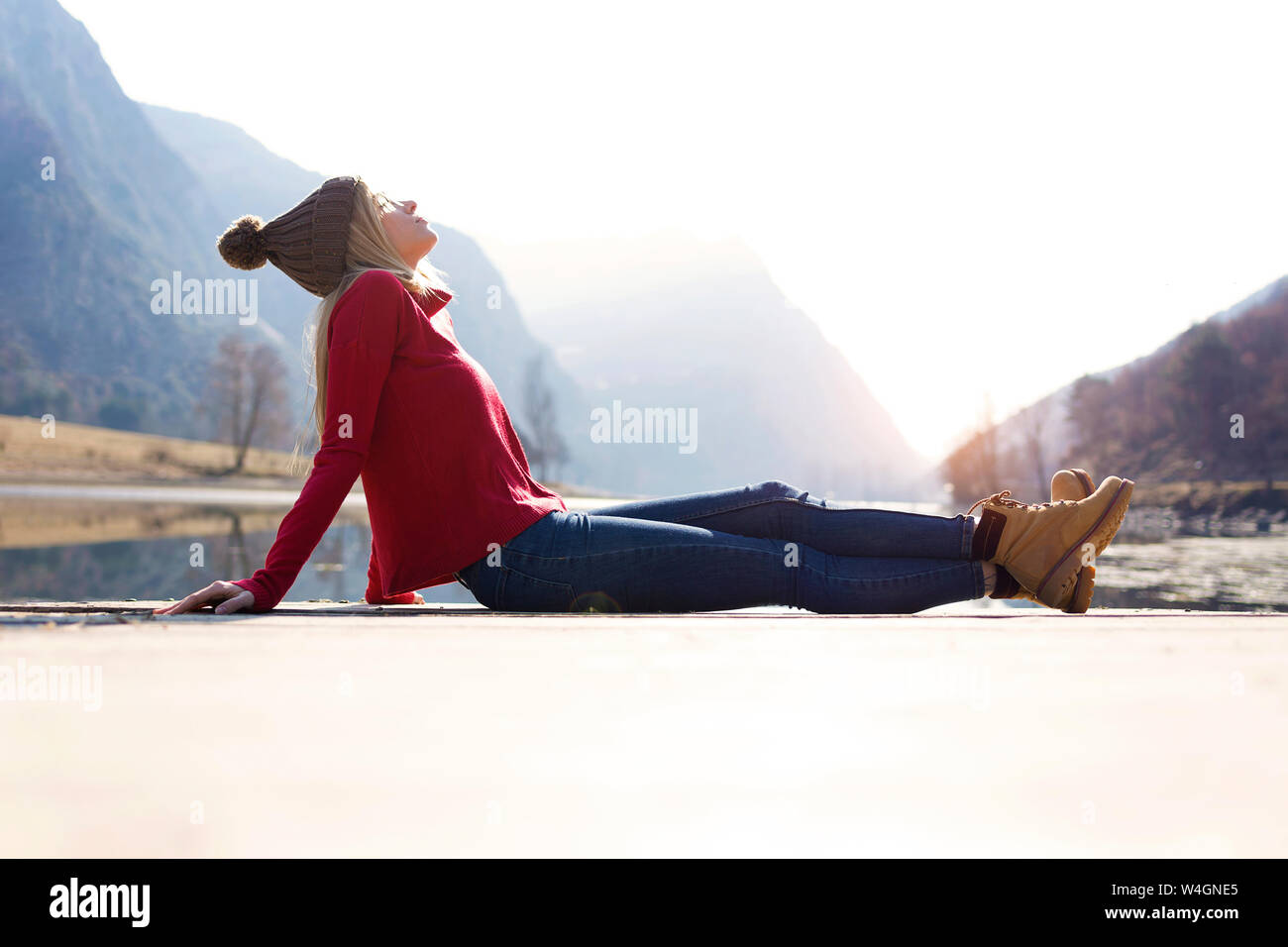 Giovane donna bionda seduta sul pontile di un lago in inverno Foto Stock