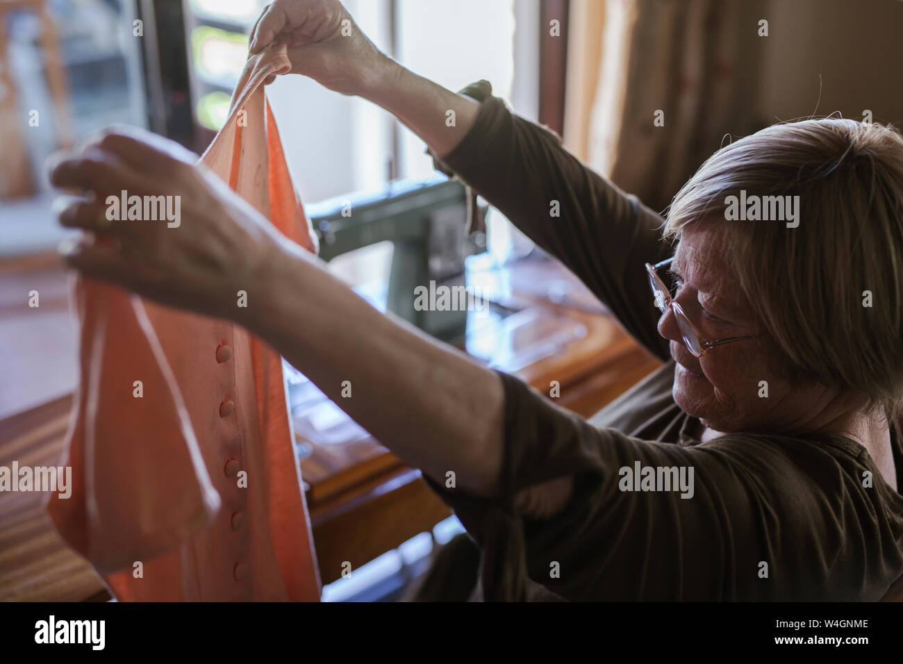 Senior donna tenendo in mano un pezzo di abbigliamento a casa Foto Stock