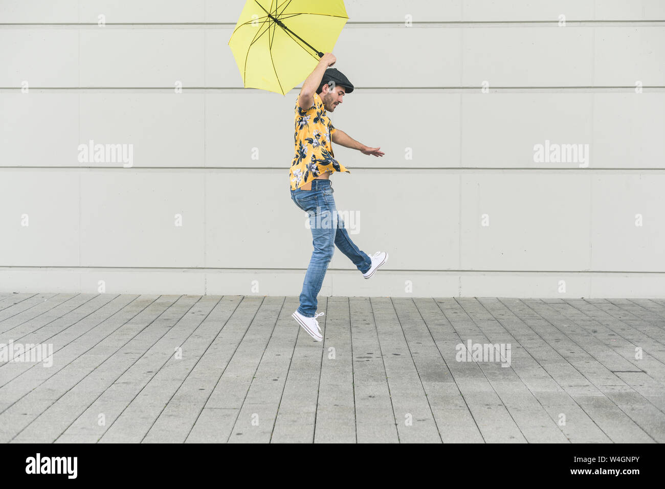Giovane uomo con aloha shirt, ballando con ombrello giallo Foto Stock