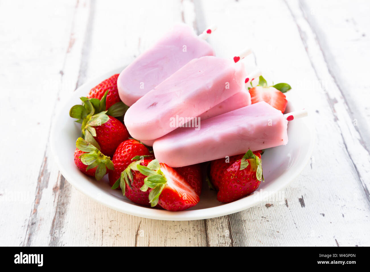 In casa di yogurt alla fragola ghiaccioli con fragole fresche in una ciotola di legno bianco Foto Stock