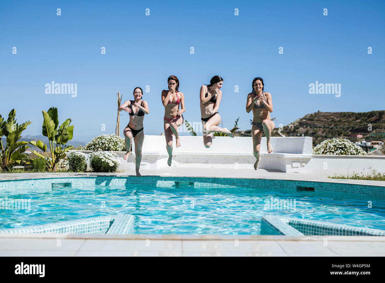 Giovani donne godendo il periodo estivo presso la piscina, saltando in acqua Foto Stock
