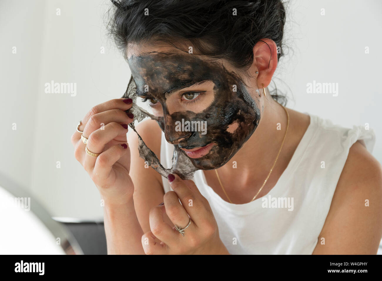 Giovane donna rimozione della maschera facciale Foto Stock