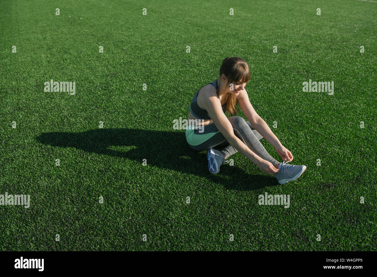 Sportive seduta sul prato e scarpe di legatura Foto Stock