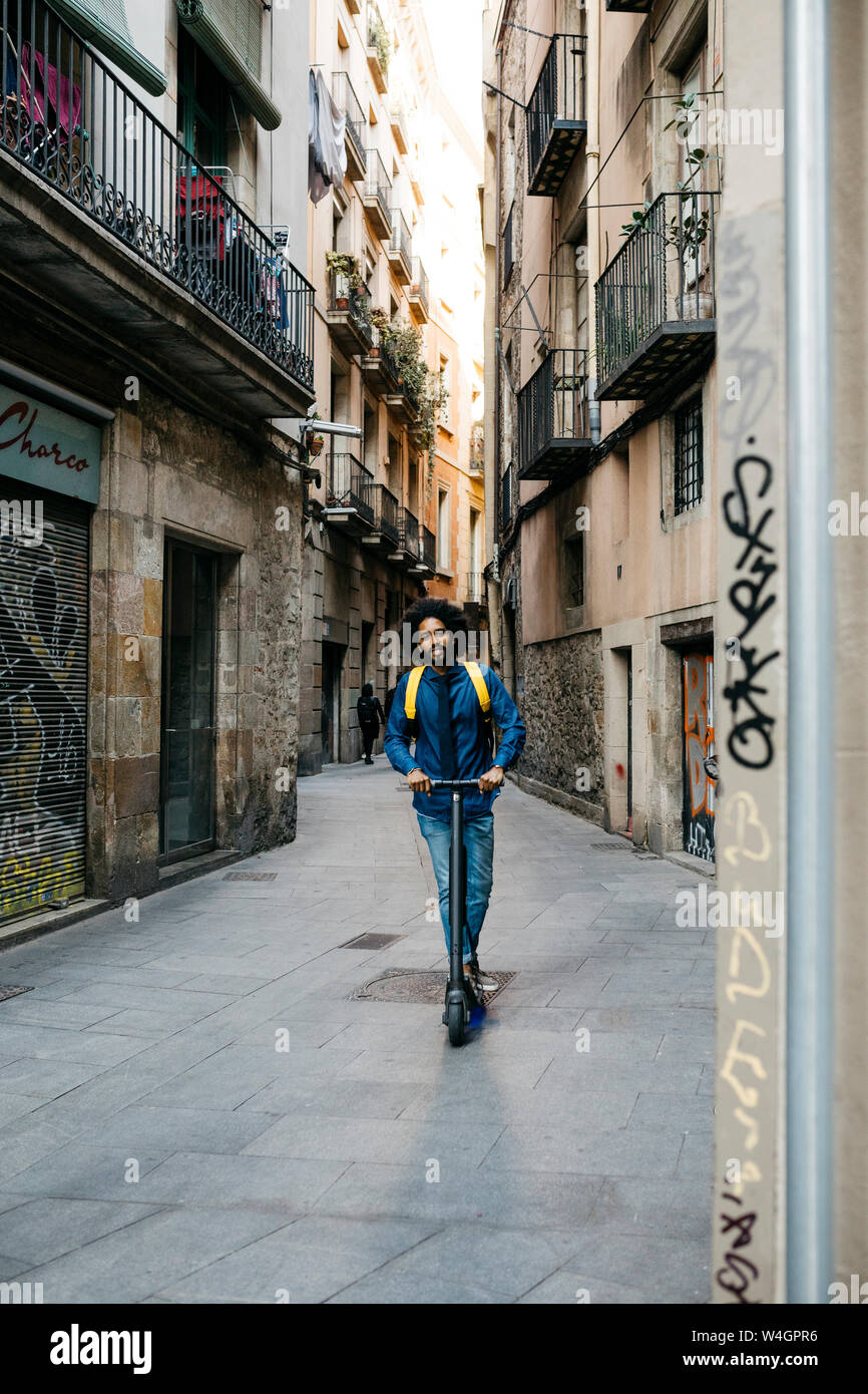 Uomo con zaino in sella al suo E-scooter in città dopo il lavoro, Barcellona, Spagna Foto Stock