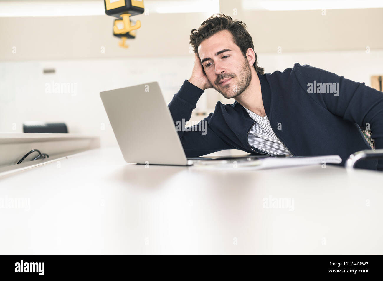 Rilassata giovane imprenditore con laptop, seduto in ufficio Foto Stock