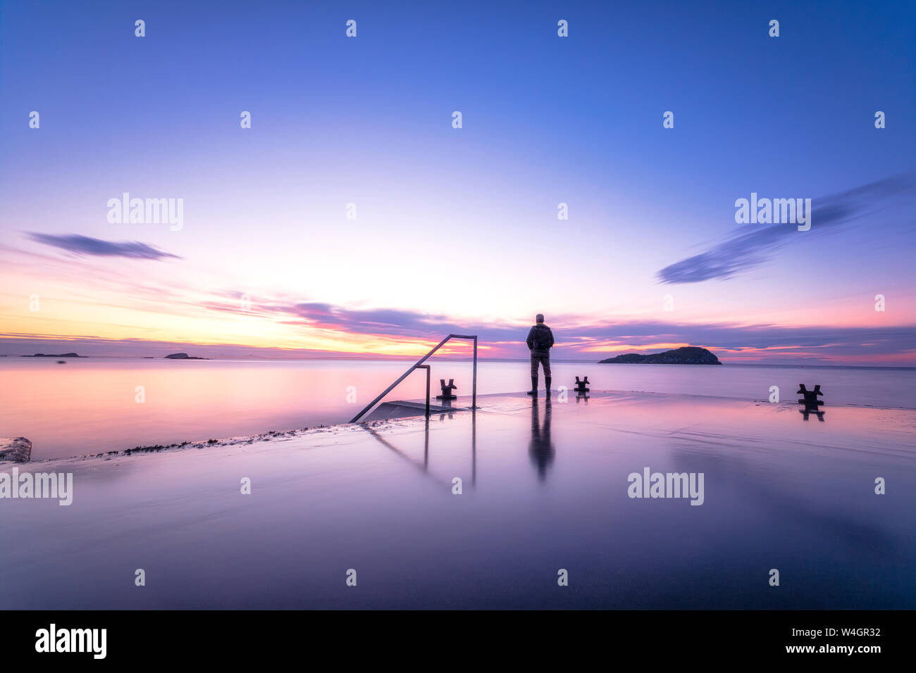 Uomo in piedi da solo sul molo del porto di guardare il tramonto, North Berwick, East Lothian, Scozia Foto Stock