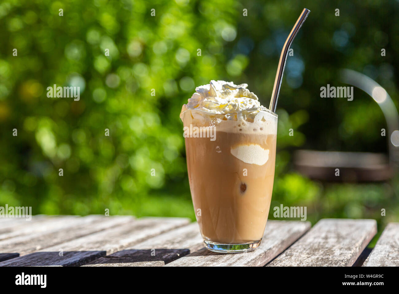 Bicchiere di caffè ghiacciato con crema di farcitura sul tavolo da giardino Foto Stock