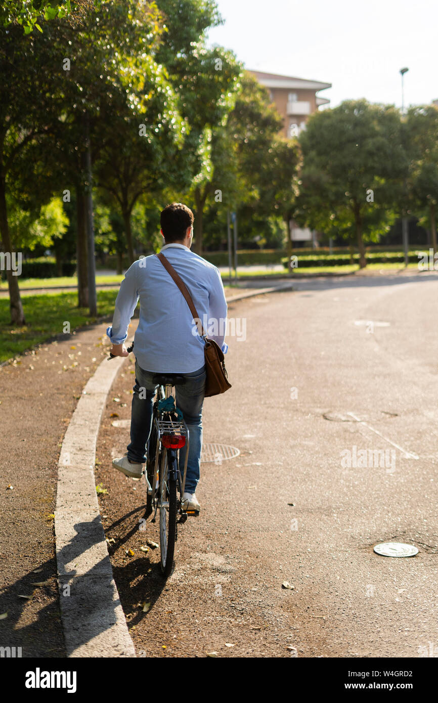 Vista posteriore del giovane uomo in sella ad una bicicletta su strada Foto Stock