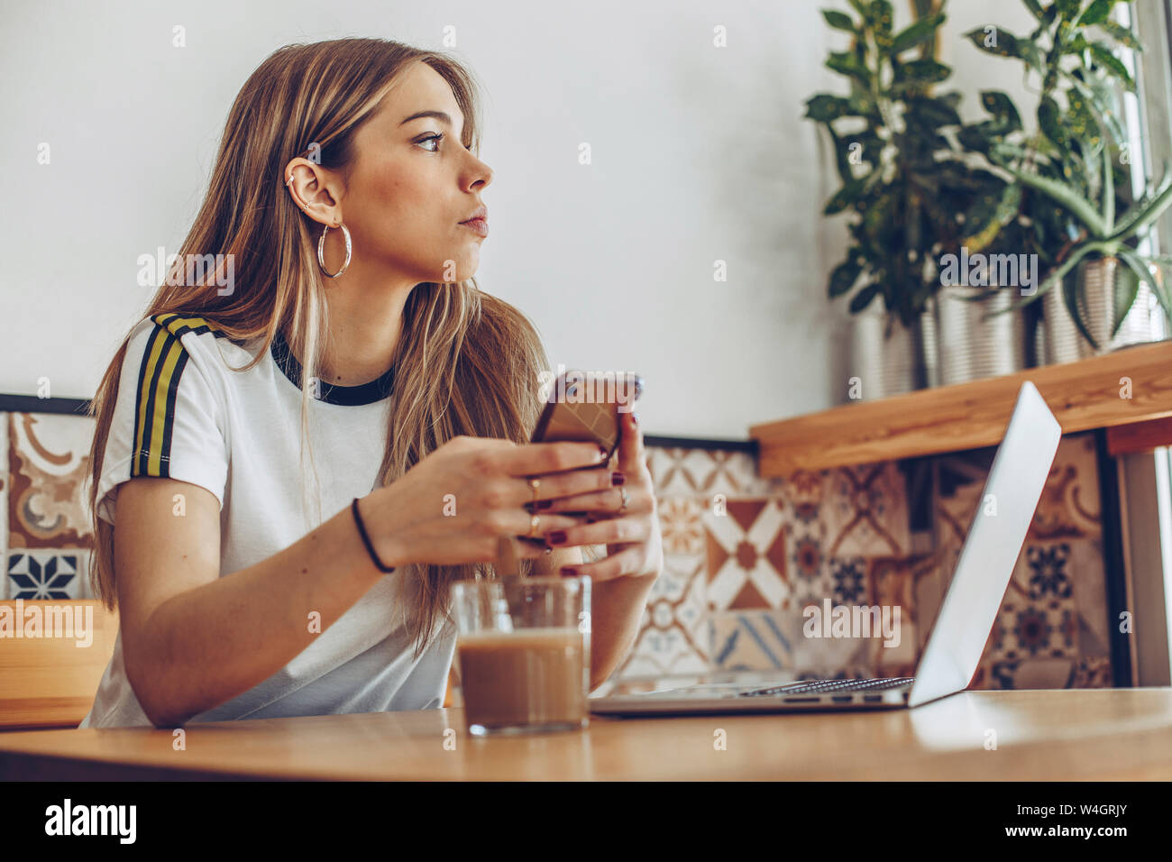 Giovane donna utilizzando il telefono cellulare e il computer portatile in cafe Foto Stock