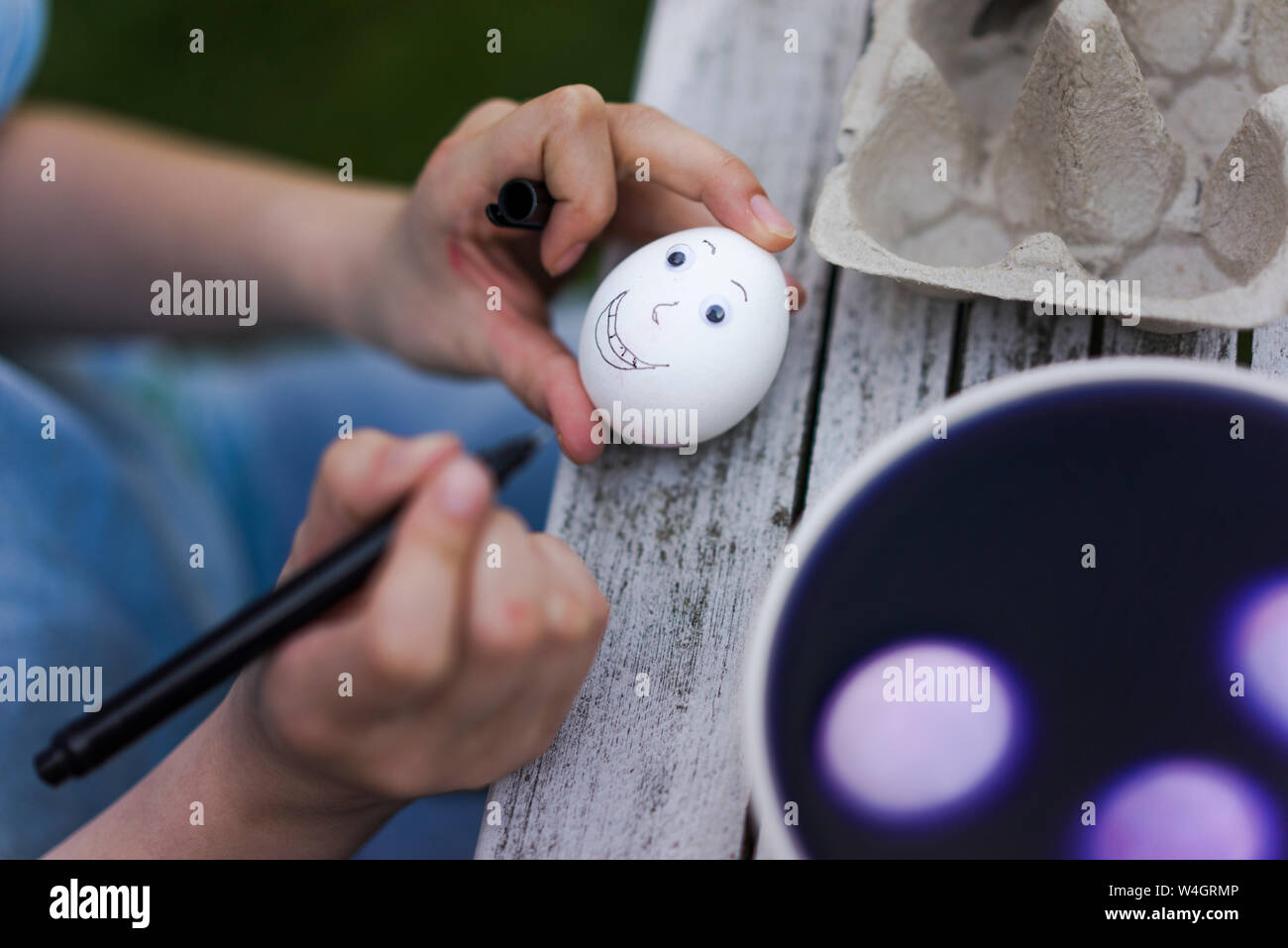 Close-up di ragazza faccia di pittura su uovo di pasqua sul tavolo da giardino Foto Stock