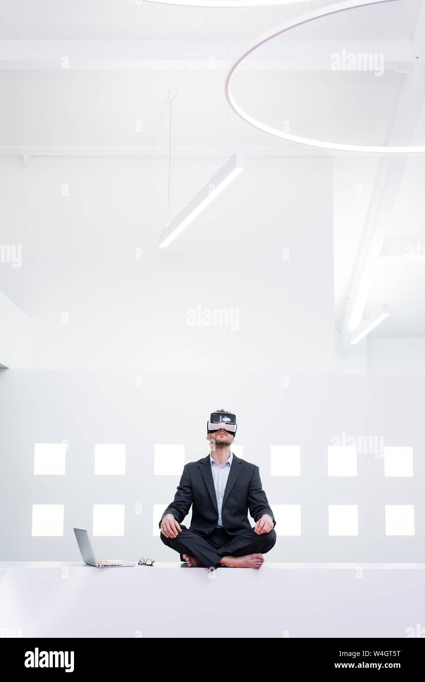 Imprenditore indossando occhiali VR in office accanto al laptop Foto Stock