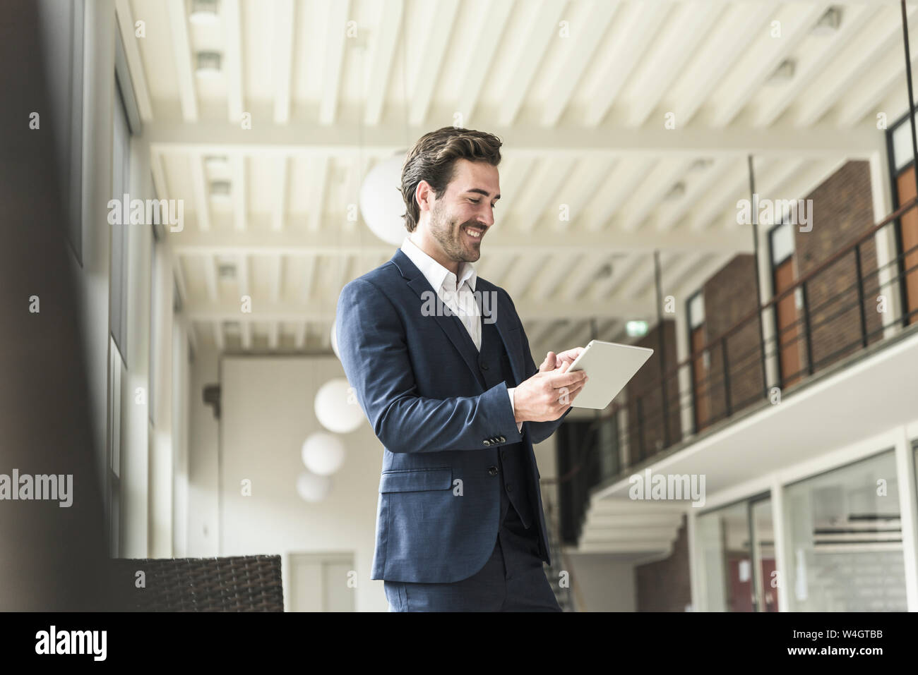 Manager di successo in piedi in un ufficio moderno edificio, utilizzando laptop Foto Stock