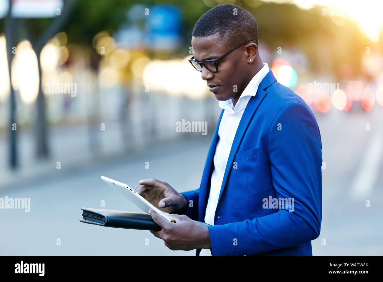 Giovane imprenditore indossare tuta blu camicia e utilizzando la sua tavoletta digitale a una via Foto Stock