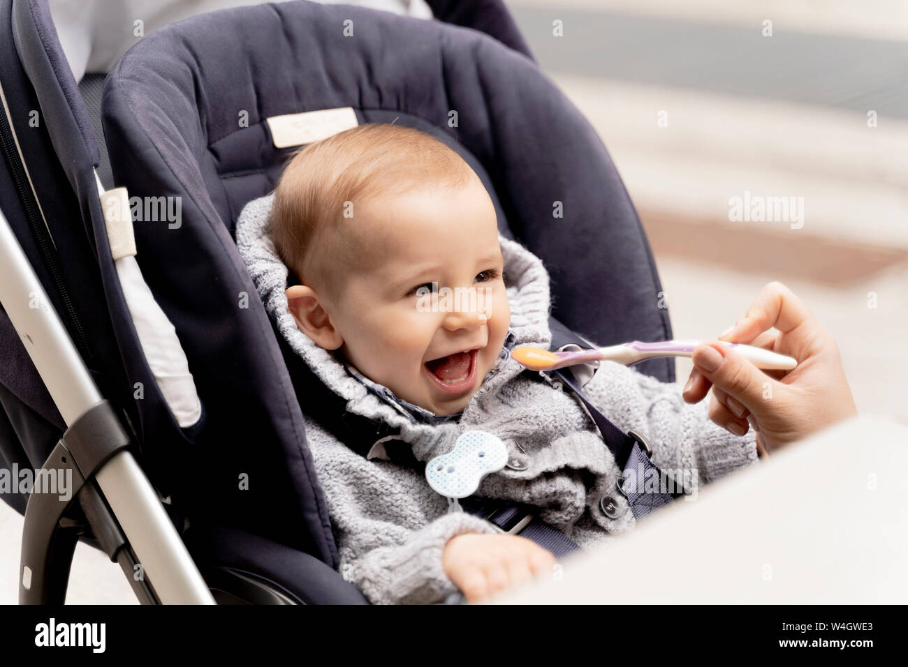 Alimentazione madre Laughing baby boy in passeggino Foto Stock