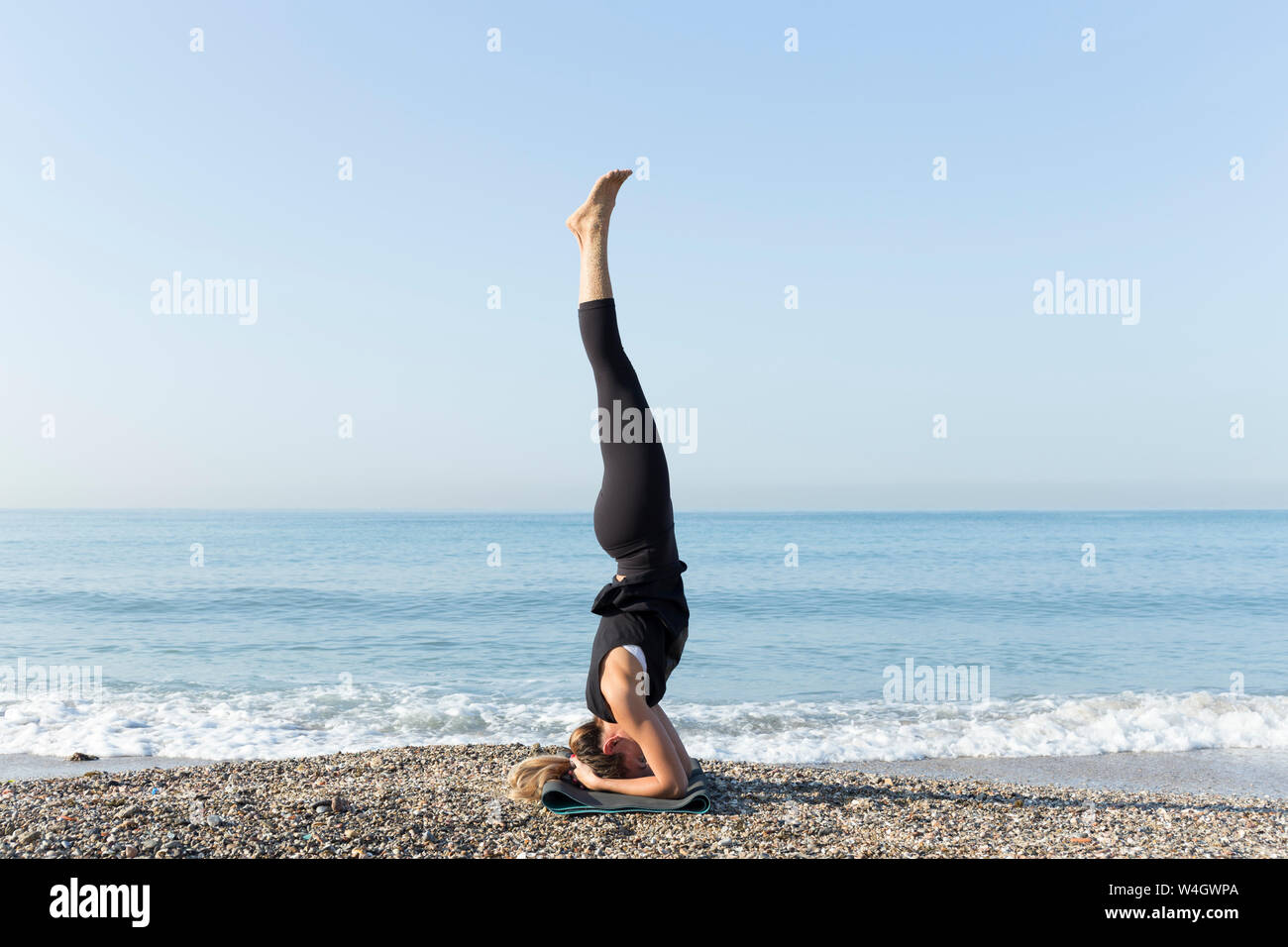 Giovane donna a praticare yoga sulla spiaggia, facendo headstand Foto Stock