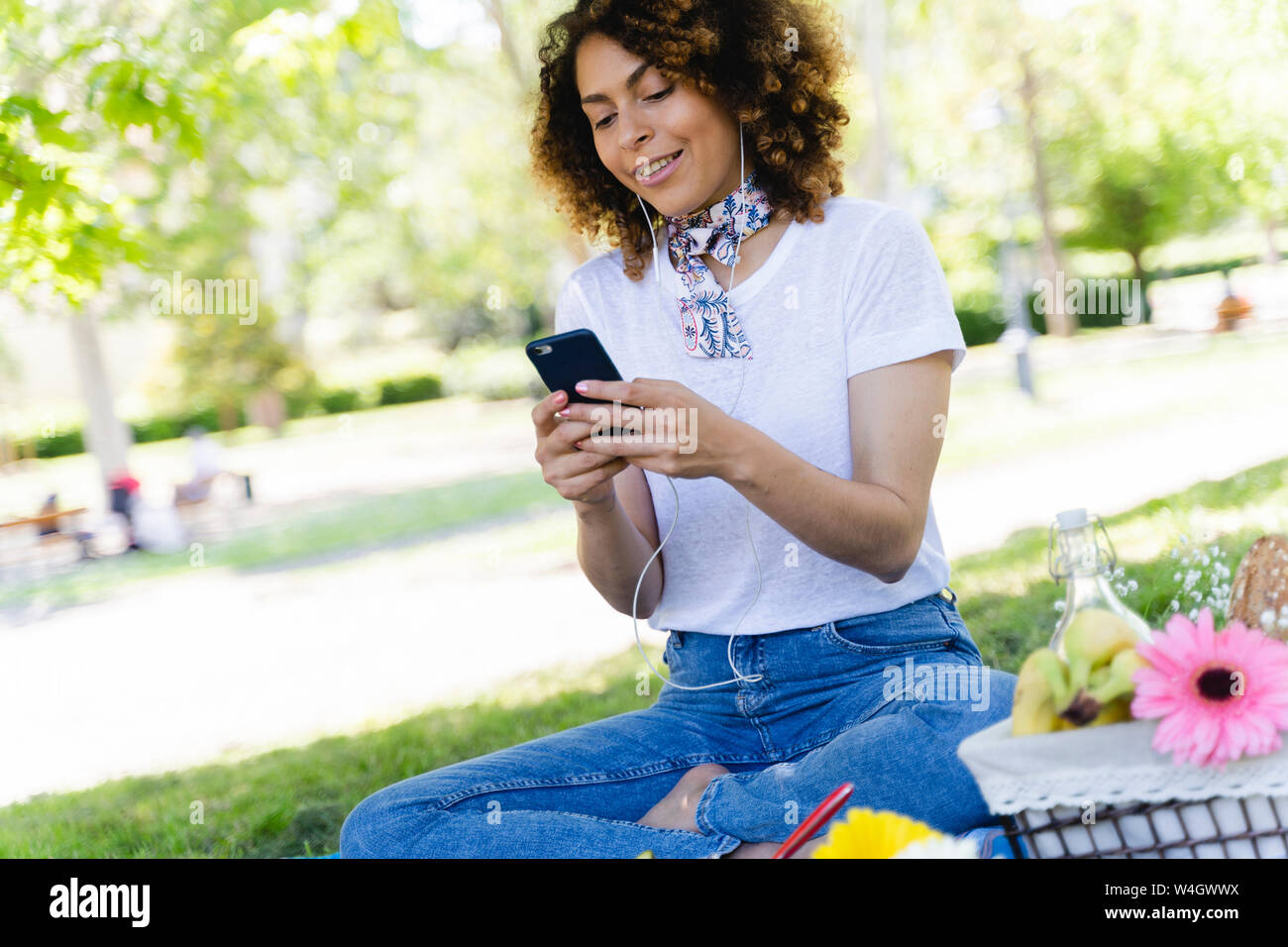 Donna rilassata con un telefono cellulare e auricolari avente un picnic nel parco Foto Stock