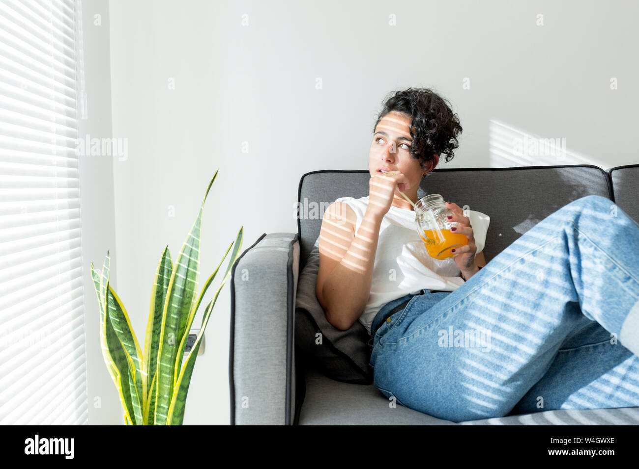 Rilassata giovane donna seduta sul divano con una bibita Foto Stock
