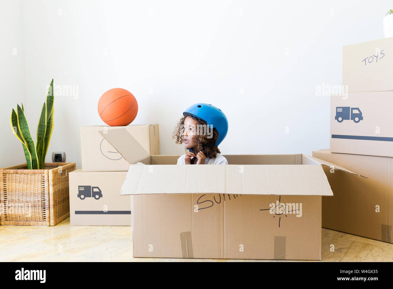 Ragazza all'interno di una scatola di cartone a new home chiusura casco per bicicletta Foto Stock