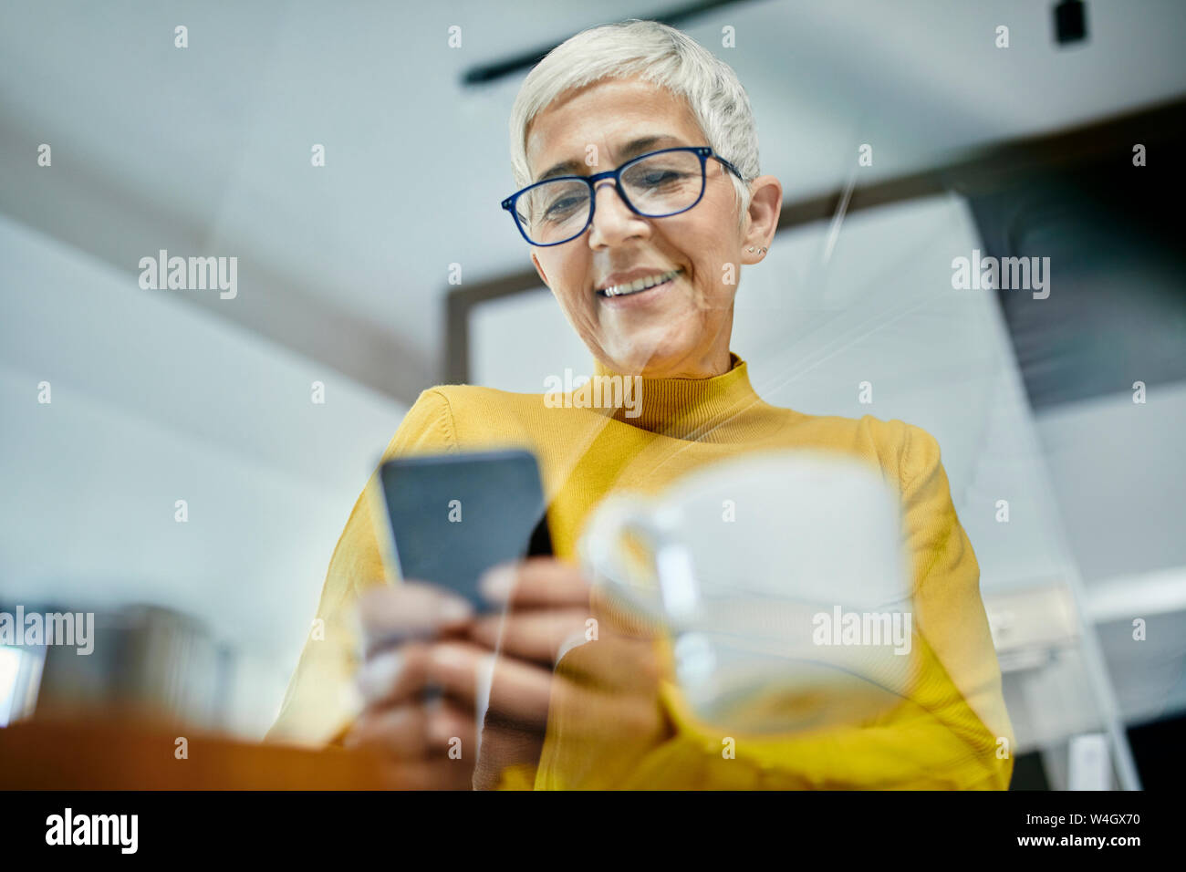 Donna senior di bere caffè, controllo messaggi di testo sullo smartphone Foto Stock