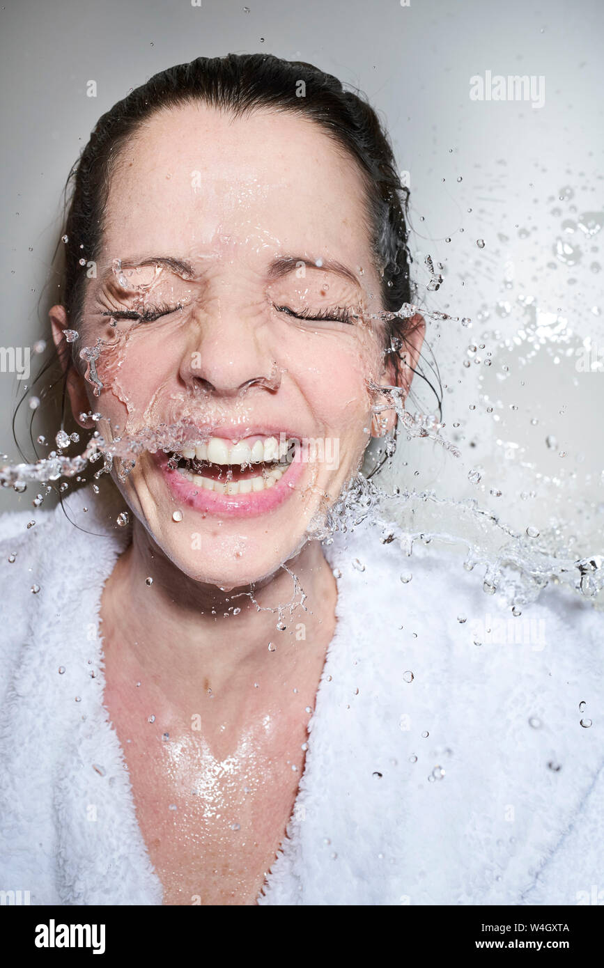 Spruzzi di acqua nel volto di donna felice in accappatoio Foto Stock