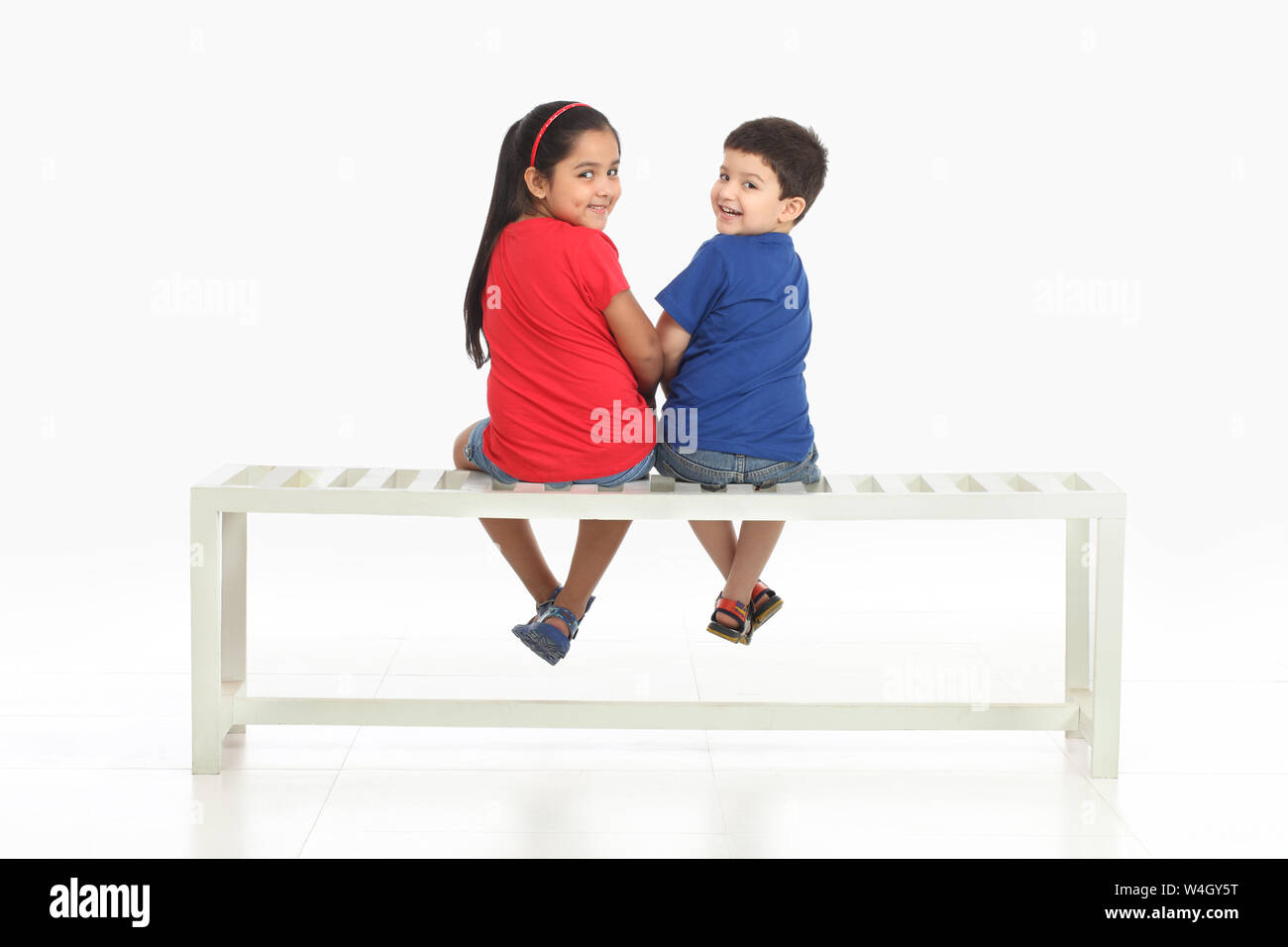 Due bambini seduti su una panchina e sorridente Foto Stock
