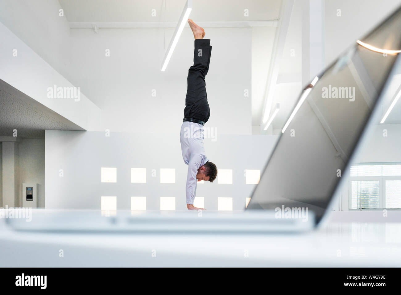 Imprenditore facendo un handstand al computer portatile in ufficio Foto Stock