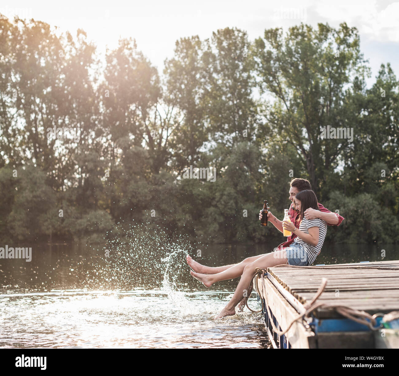 Felice coppia giovane avente un drink e spruzzi con acqua sul pontile di un lago in remoto Foto Stock