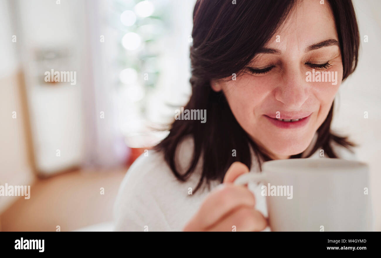 Donna matura in un bagno a casa gustando una tazza di caffè Foto Stock