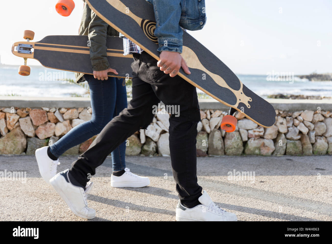 Coppia giovane con longboards passeggiate sul lungomare, vista parziale Foto Stock
