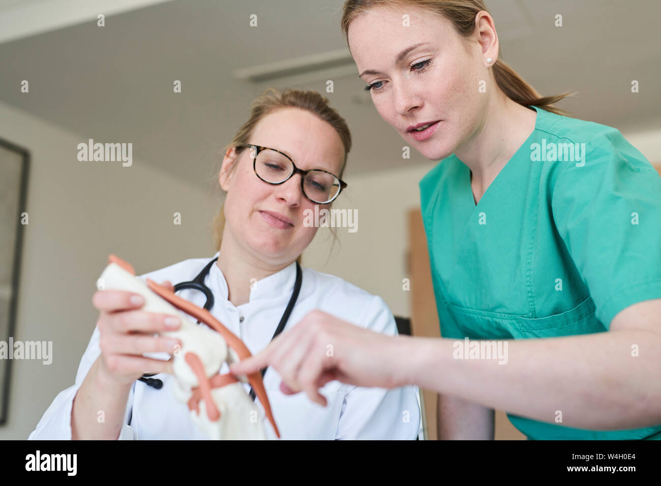 Medico donna e donna in frega con ginocchio parlare di modello Foto Stock