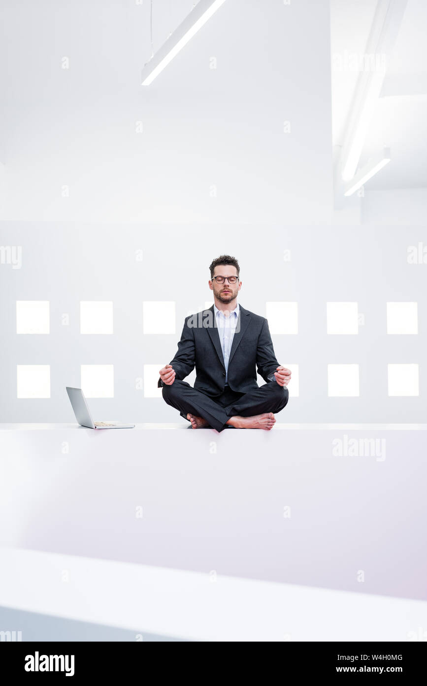 Imprenditore fare yoga in ufficio accanto al laptop Foto Stock