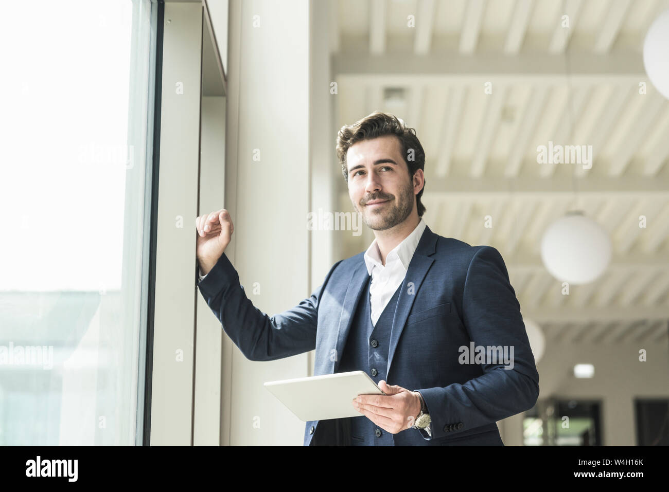 Manager di successo in piedi in un ufficio moderno edificio, utilizzando laptop Foto Stock