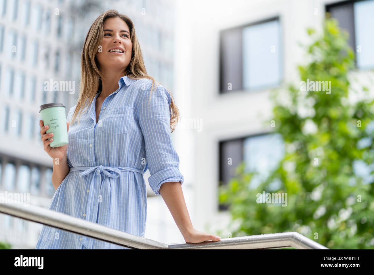 Giovane imprenditrice con caffè per andare cup, edificio per uffici in background Foto Stock