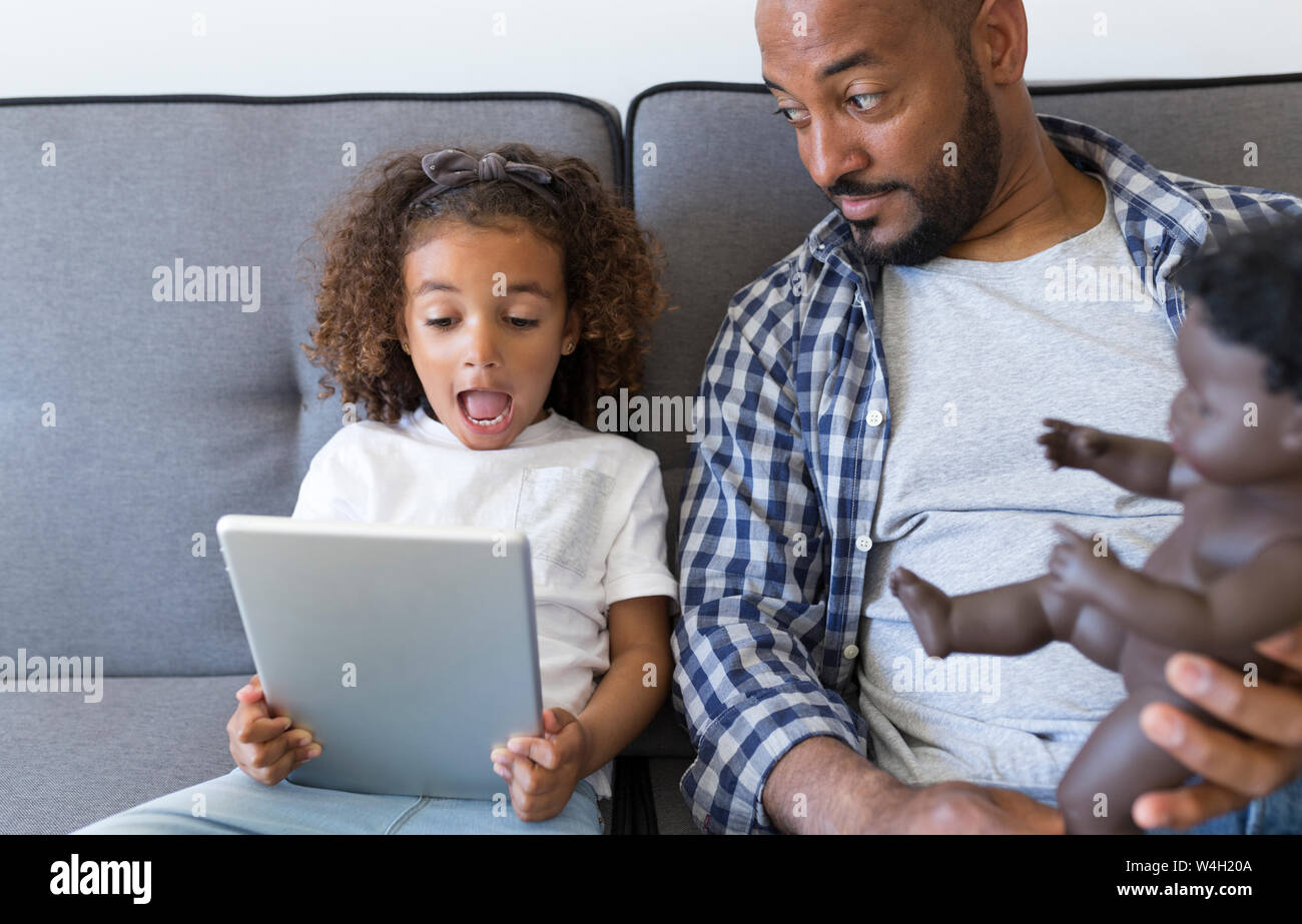 Padre e figlia eccitato seduti sul divano di casa guardando tablet Foto Stock