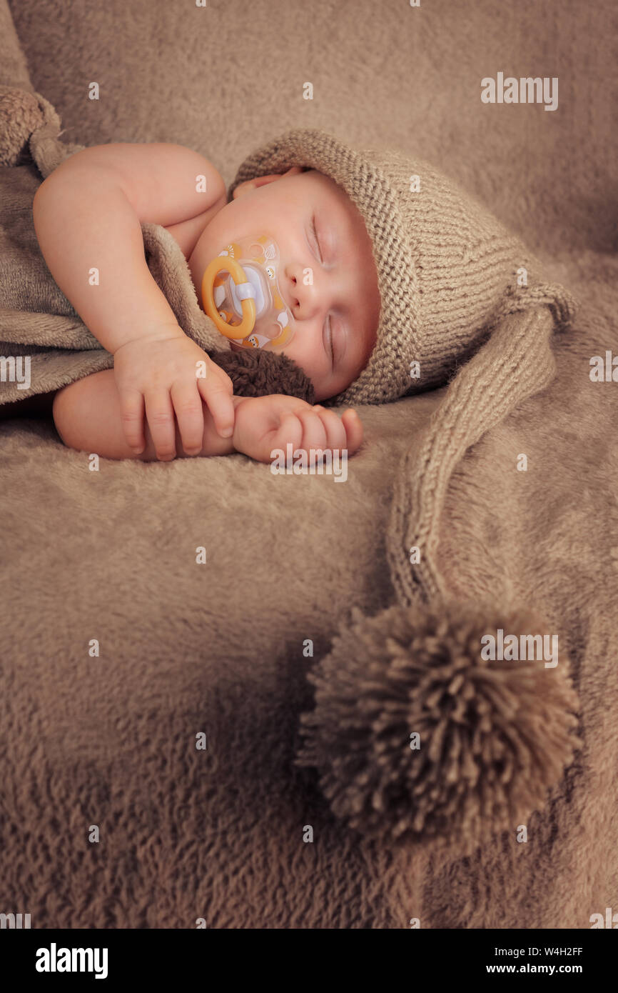 Bambino con il succhietto in berretto lavorato a maglia con pom pom. Formato verticale. Foto Stock