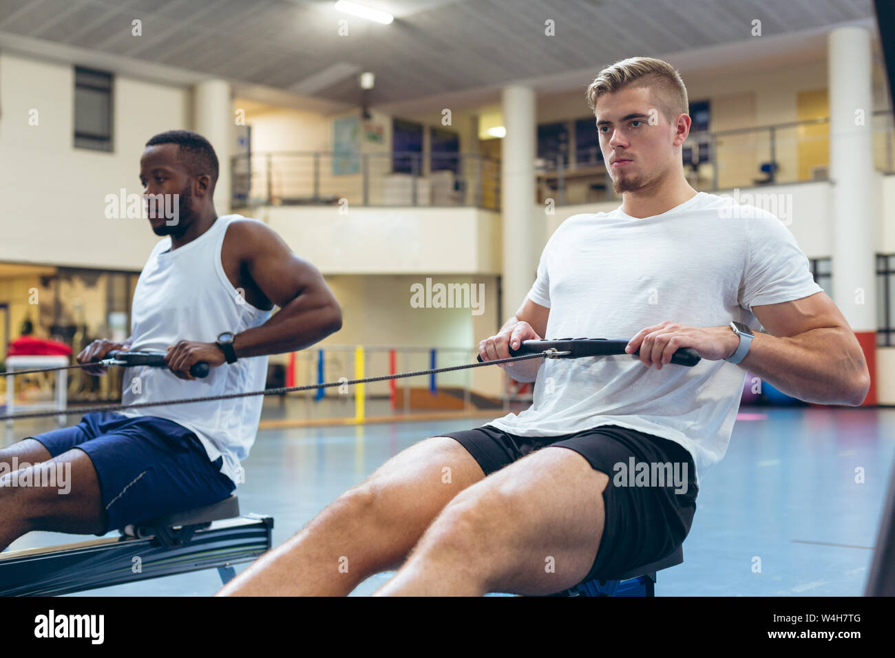 Gli atleti di sesso maschile che esercitano con vogatore in studio fitness Foto Stock