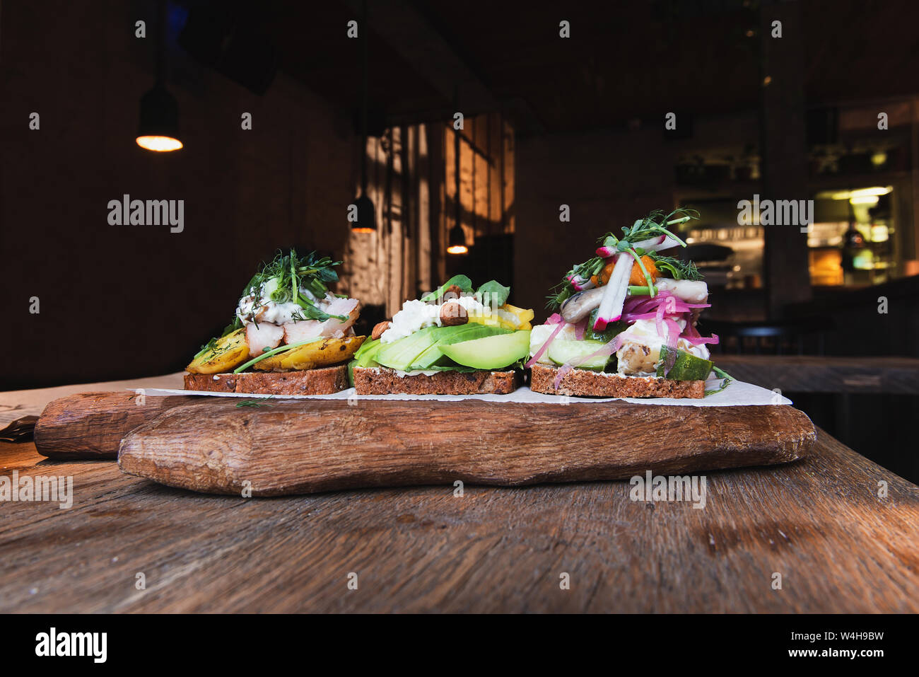 Antipasti scandinavo con il pane su una tavola di legno e legno pensione alimentare in elegante caffe'. Il cibo fatto con avocado, formaggio, mandorle, aringa, una patata Foto Stock