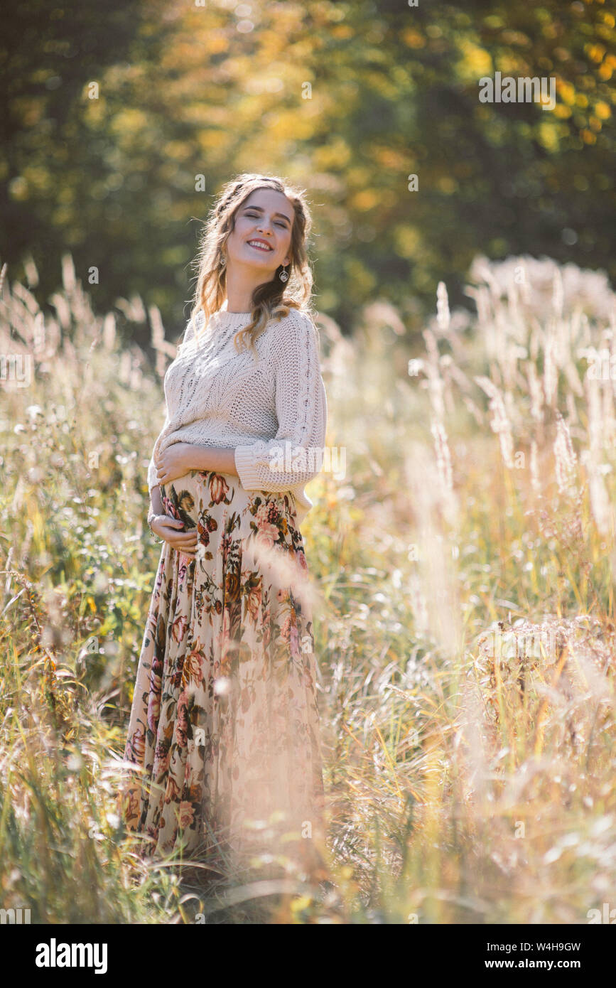 Sorridente bella donna incinta con gli occhi chiusi nel campo d'autunno. Foto Stock
