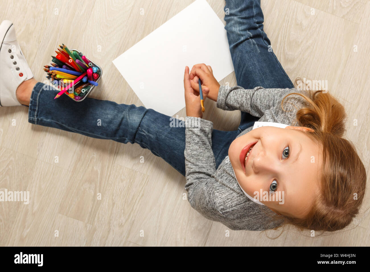 Vista superiore della bambina di pittura, guardando la fotocamera e seduto sul pavimento nella sua stanza in casa. Foto Stock