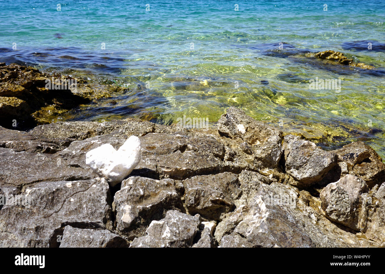 Costa del mare in estate con interessanti pietre e rocce sulla parte anteriore e il turchese e il blu del mare di acqua in background Foto Stock