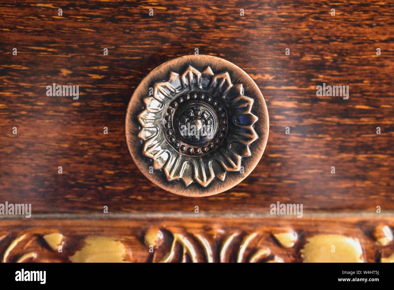 Pomello circolare in metallo con disegno floreale geometrico inciso su una cassettiera, con un ricco fondo in legno caldo. Foto Stock