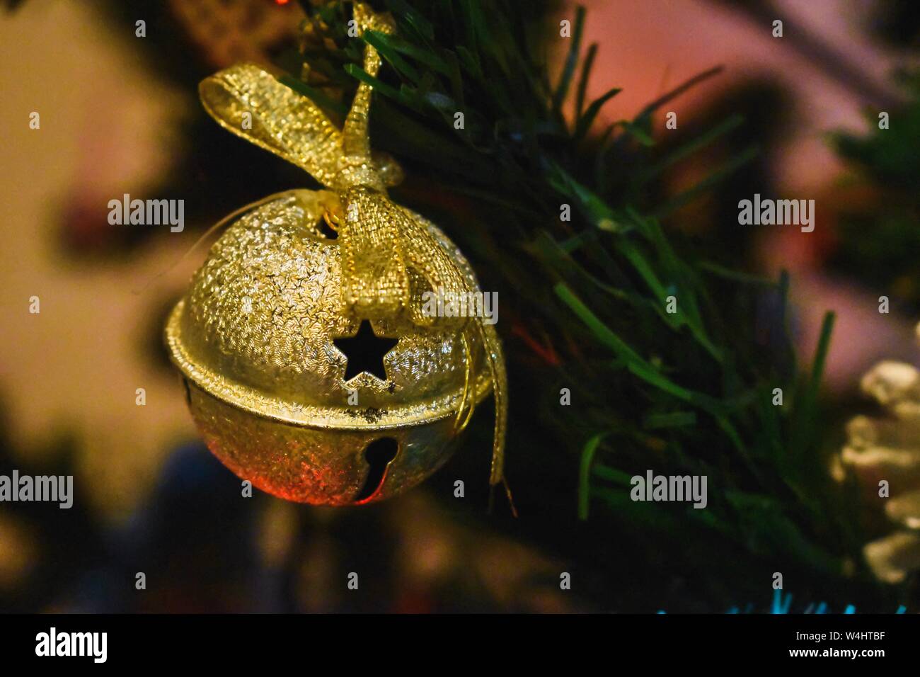 Primo piano di un ornamento a campana dorata con nastro, appeso su un albero di Natale in una casa di famiglia a dicembre. Foto Stock