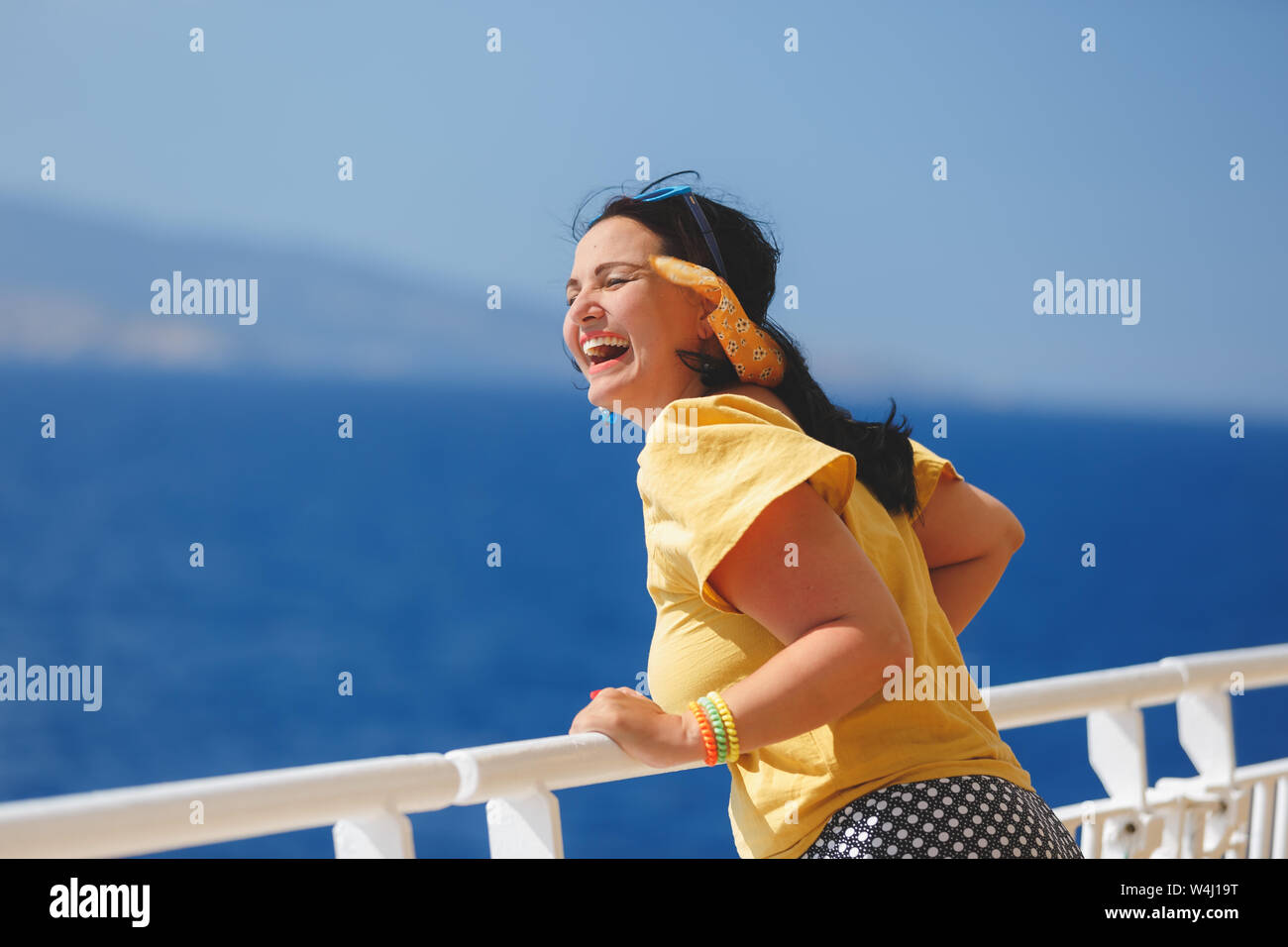 Donna felice su una vacanza in crociera. in piedi sul ponte della nave da crociera, vento forte i suoi capelli Foto Stock