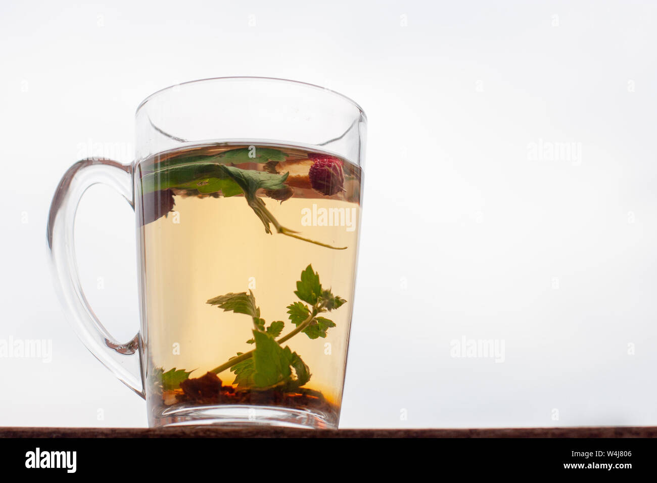 Ancora vita cup con tè alle erbe. Cielo bianco sullo sfondo. Fragola foglie e bacche sono flottanti in tazza. Vista laterale. Foto Stock