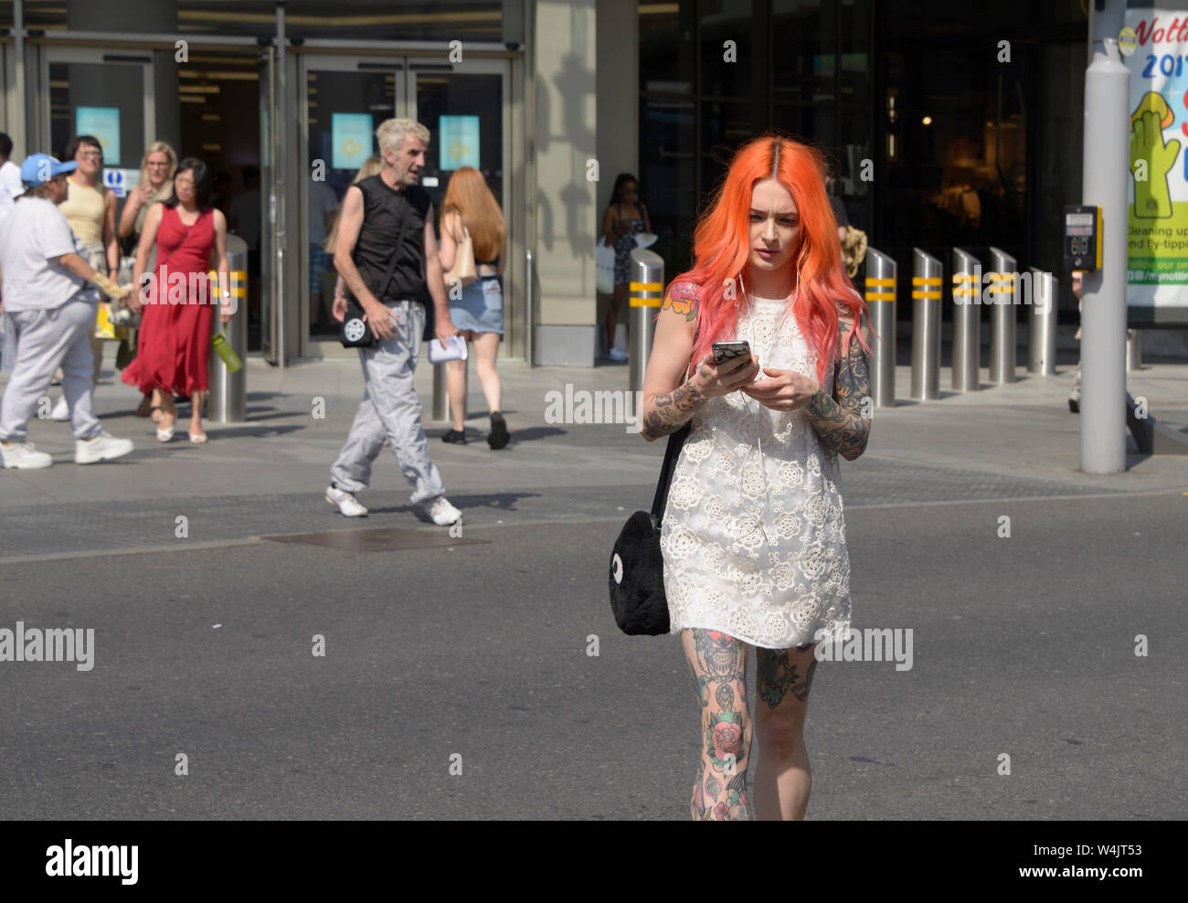Ragazza con i capelli arancione,& tatuaggi attraversamento strada sul telefono Foto Stock