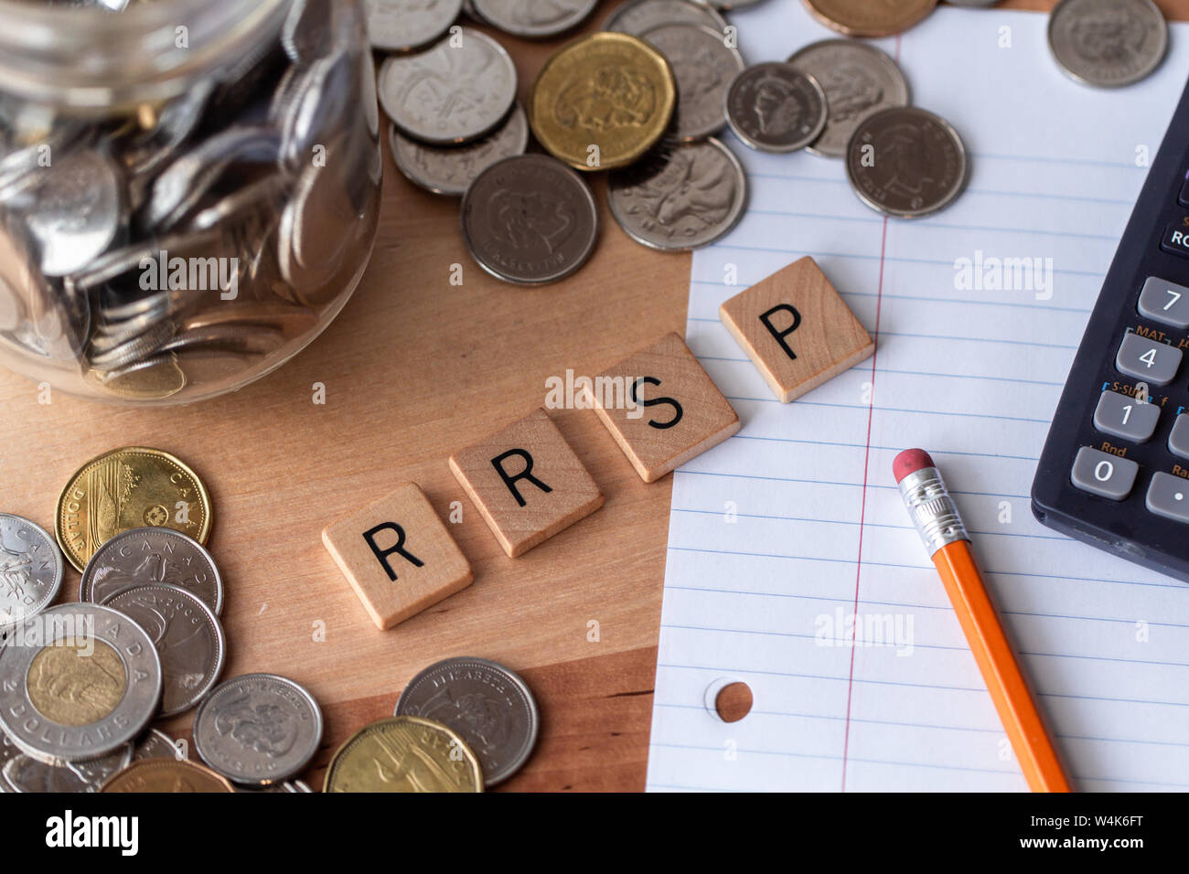 "RRSP' (registrati Piano di risparmio previdenziale) enunciato nella lettera in legno piastrelle con denaro, carta, matita e calcolatrice che circonda la parola. Foto Stock