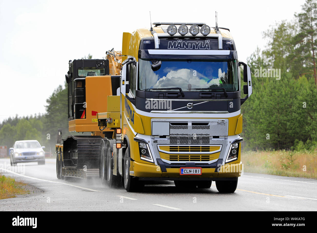 Raasepori, Finlandia. Luglio 5, 2019. Volvo FH16 semi rimorchio di E E E Mantyla Ky cale Cat 325F. escavatore idraulico come ampia carico su strada bagnata in caso di pioggia. Foto Stock