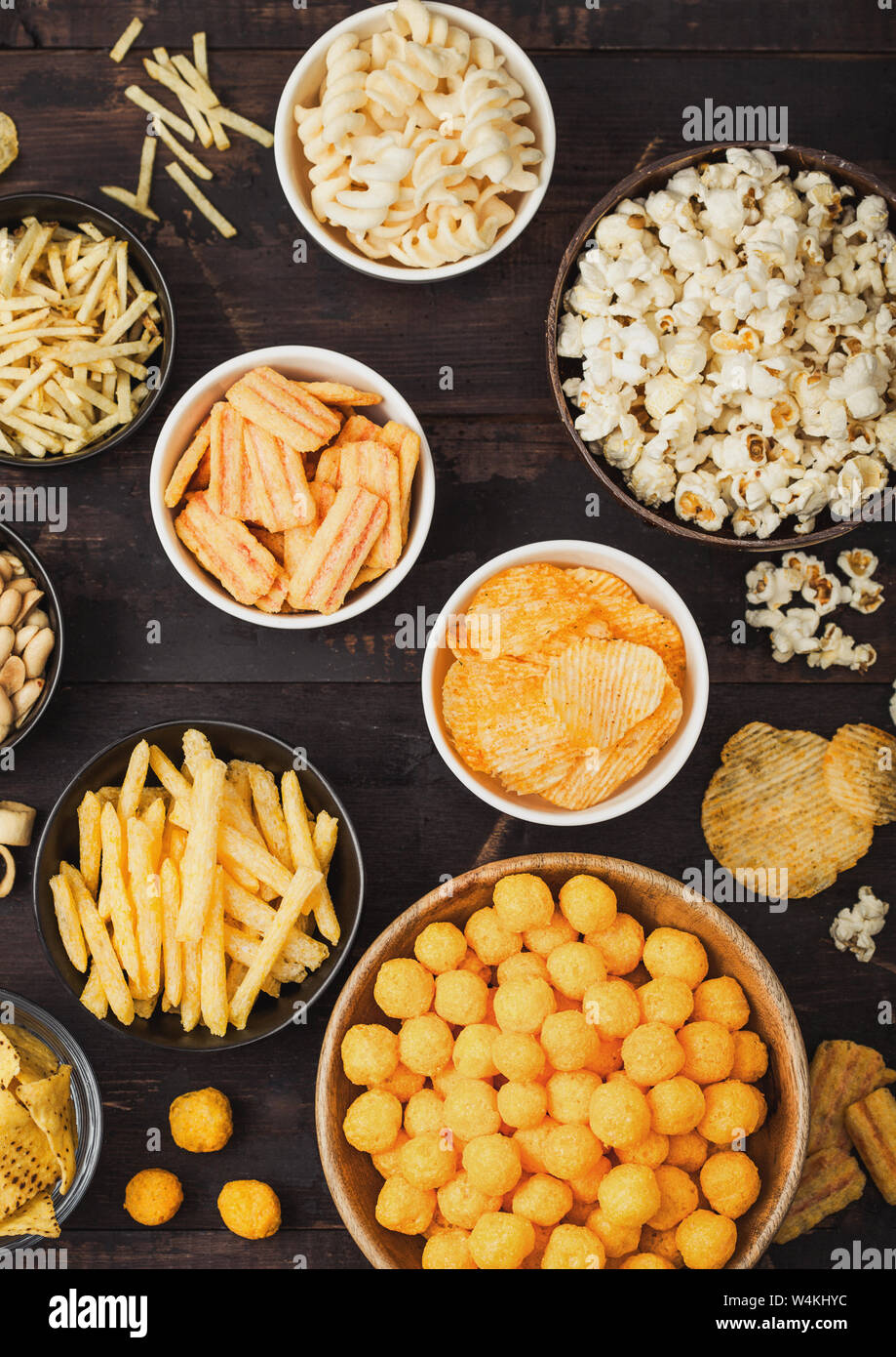 Tutti i classici snack di patate con arachidi, popcorn e anelli di cipolla  e salati pretzel nella ciotola piastre su legno. Ghirigori con bastoni e  patatine e cr Foto stock - Alamy